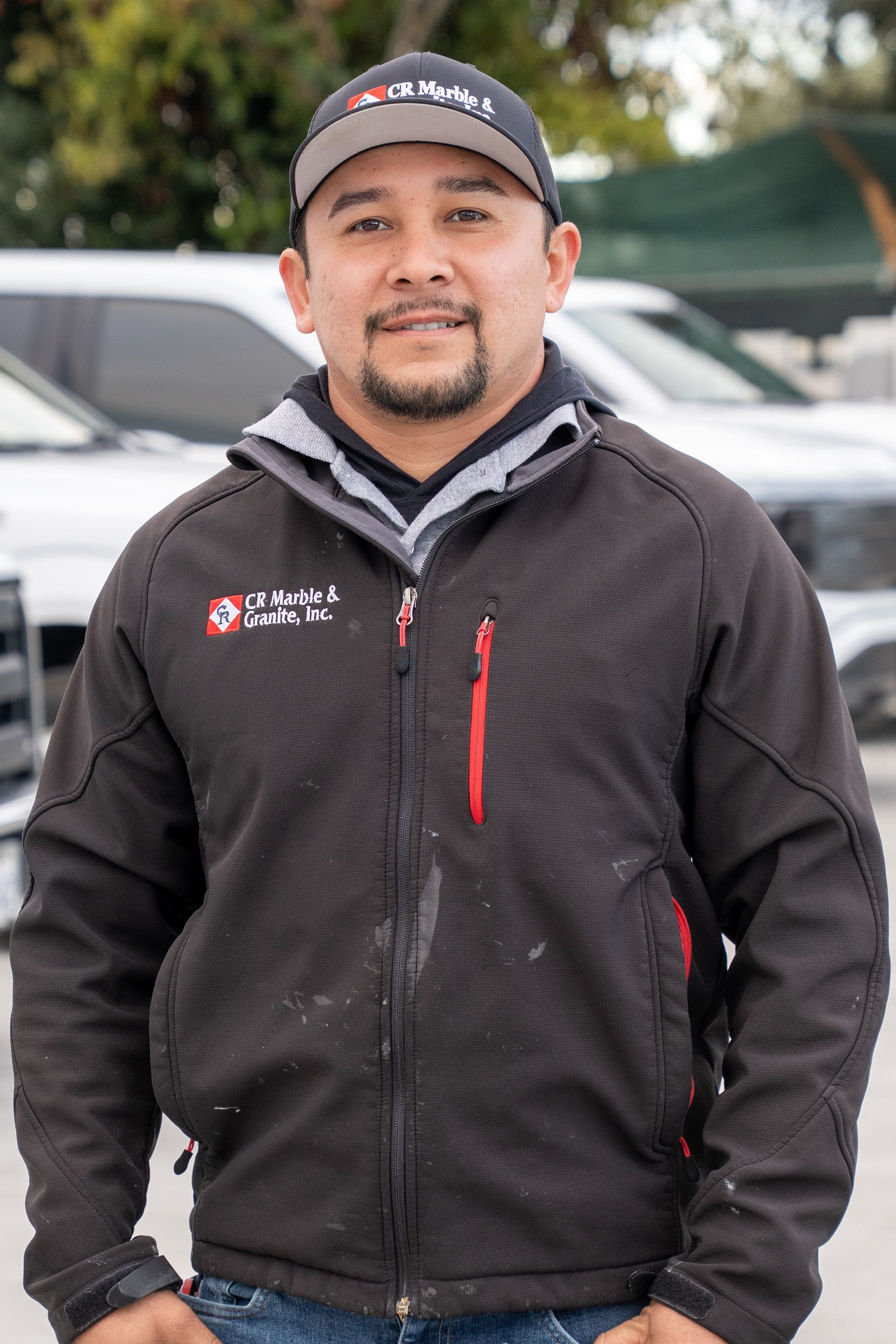 A man wearing a black jacket and a hat is standing in a parking lot.