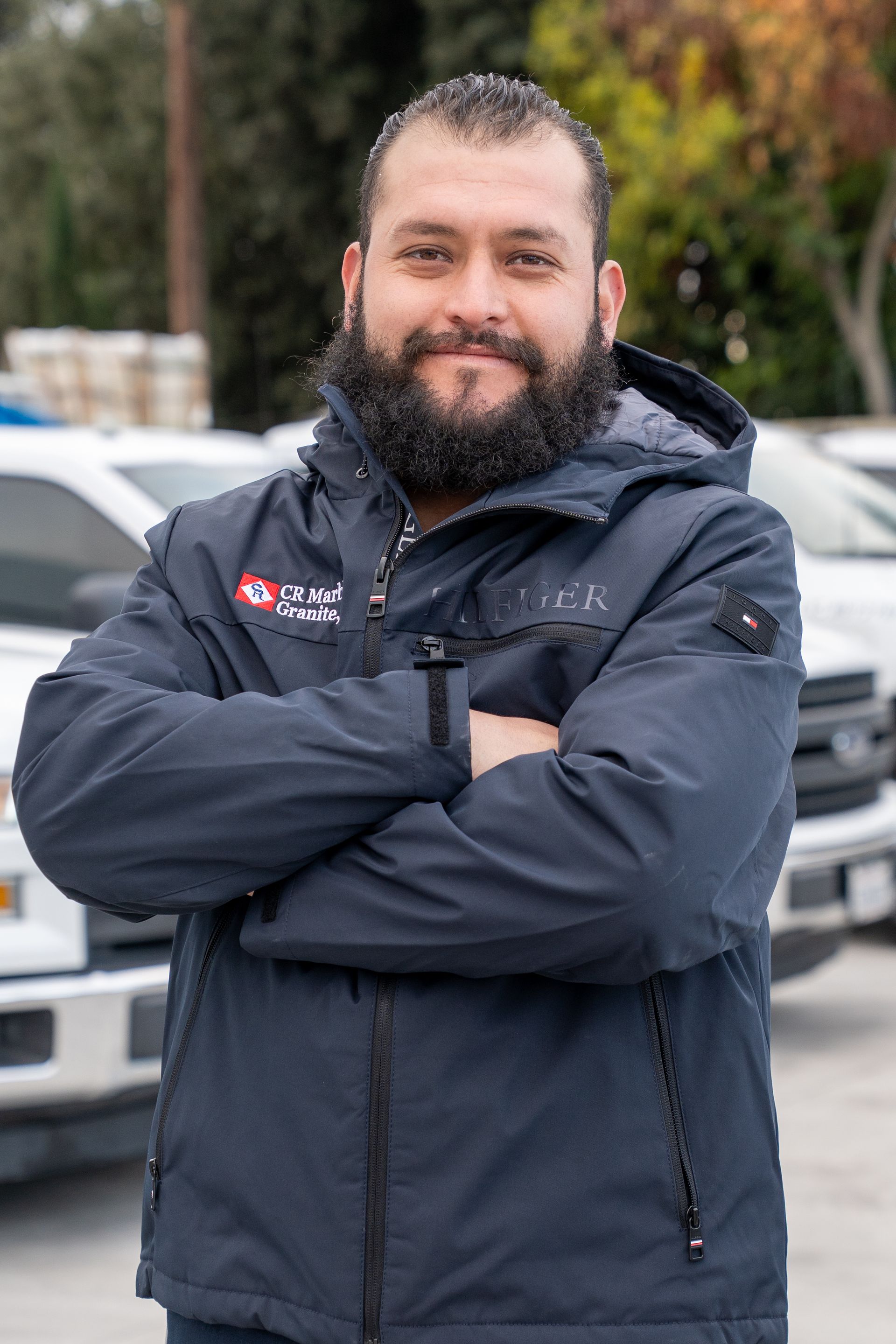 A man with a beard is standing in front of a truck with his arms crossed.