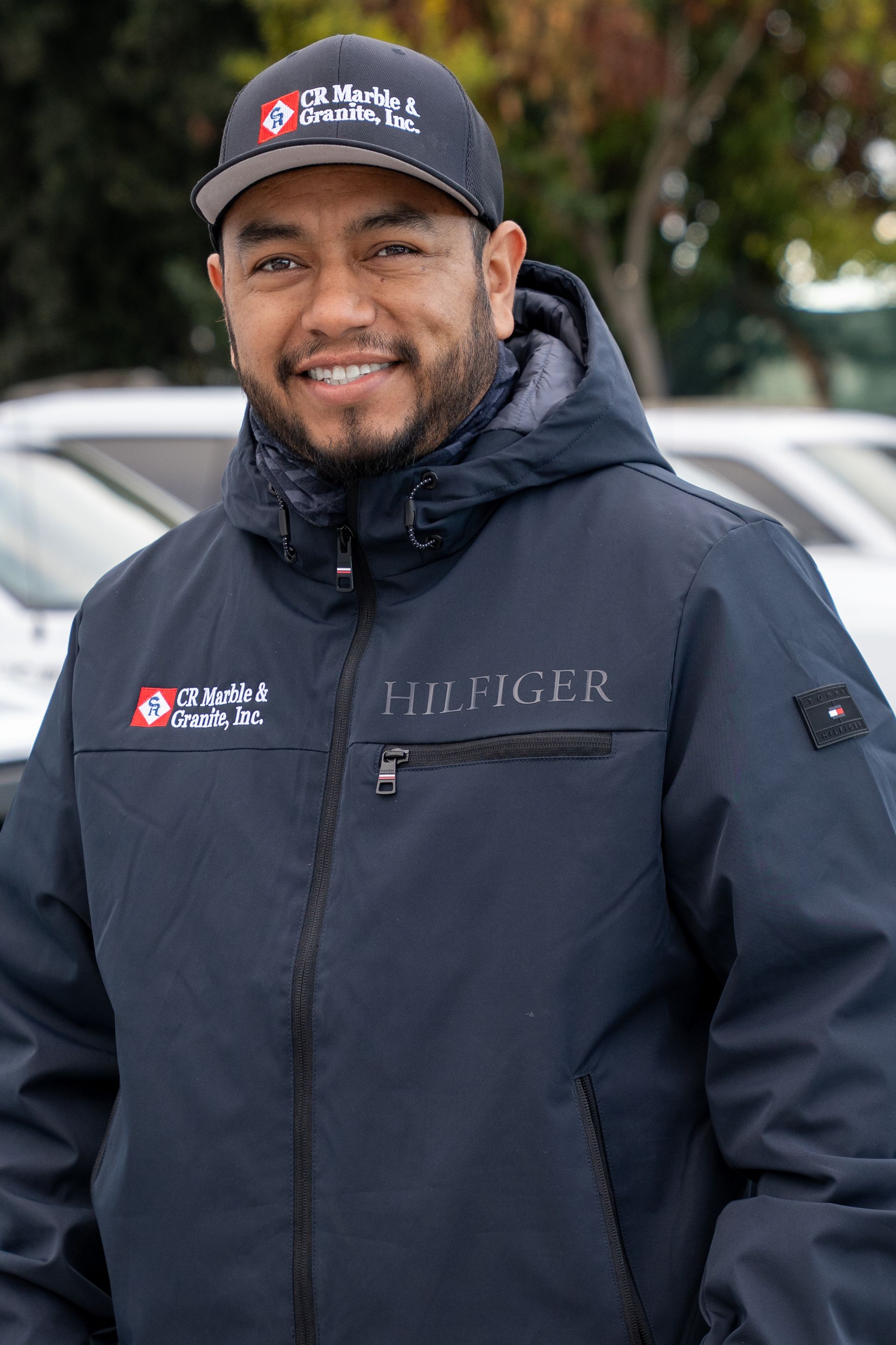 A man wearing a hat and a jacket is standing in front of a parking lot.
