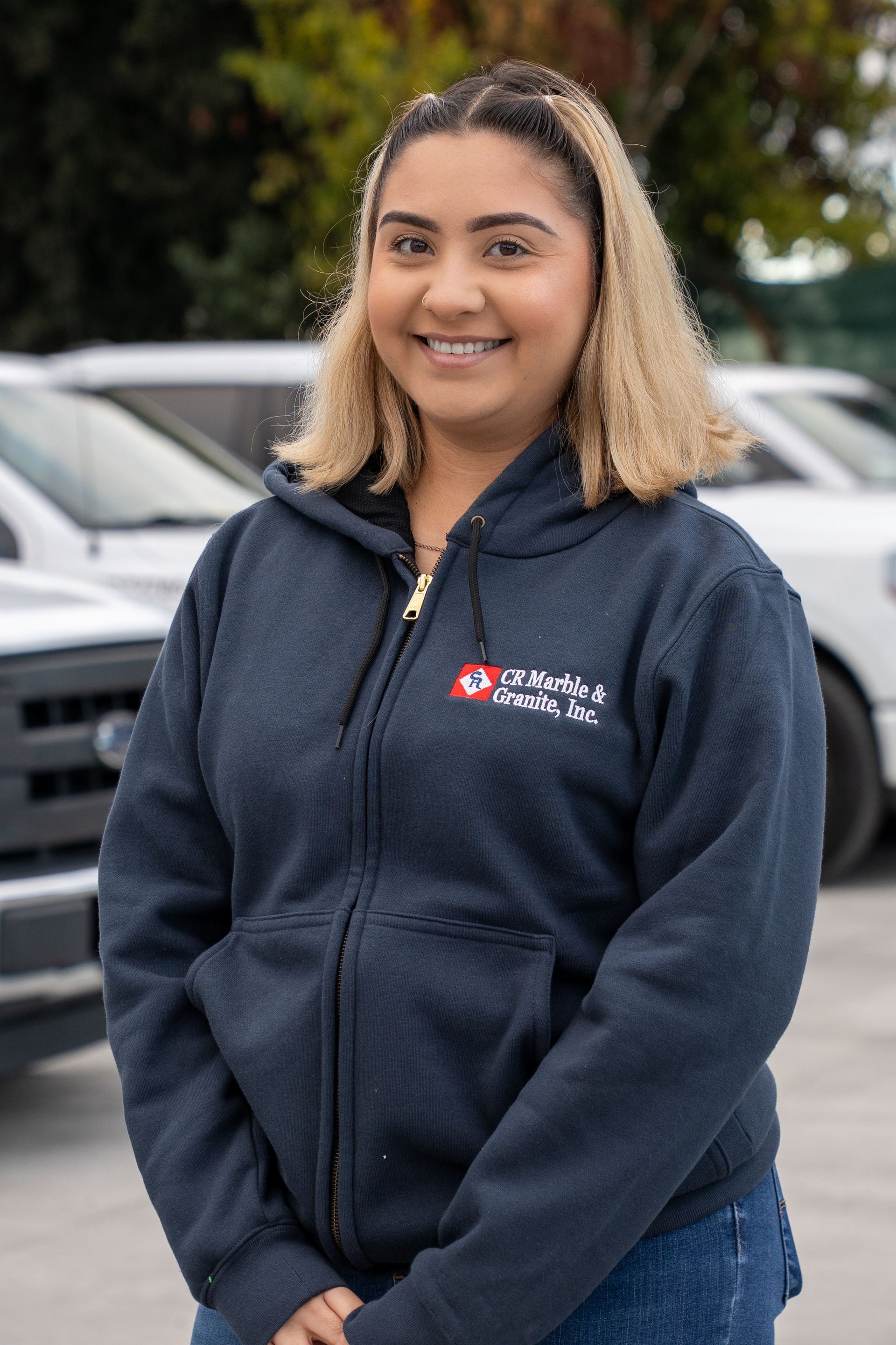 A woman wearing a blue hoodie is standing in front of a row of cars.
