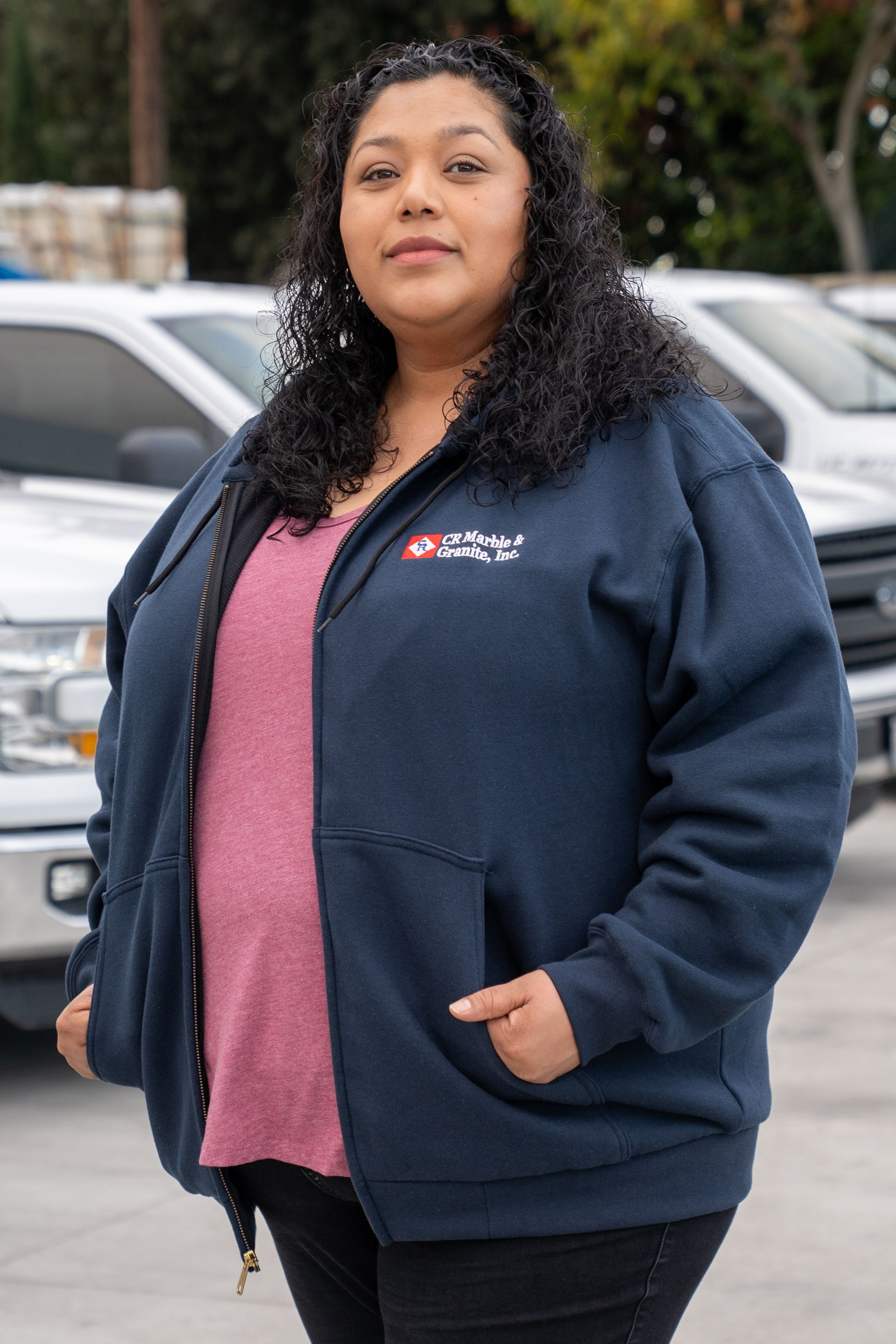A woman in a blue hoodie is standing in front of a row of cars.