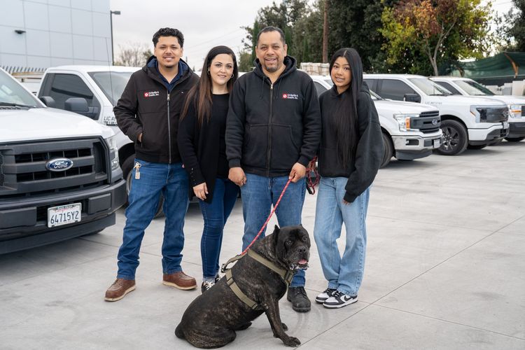 A group of people standing next to a black dog in front of a row of trucks.