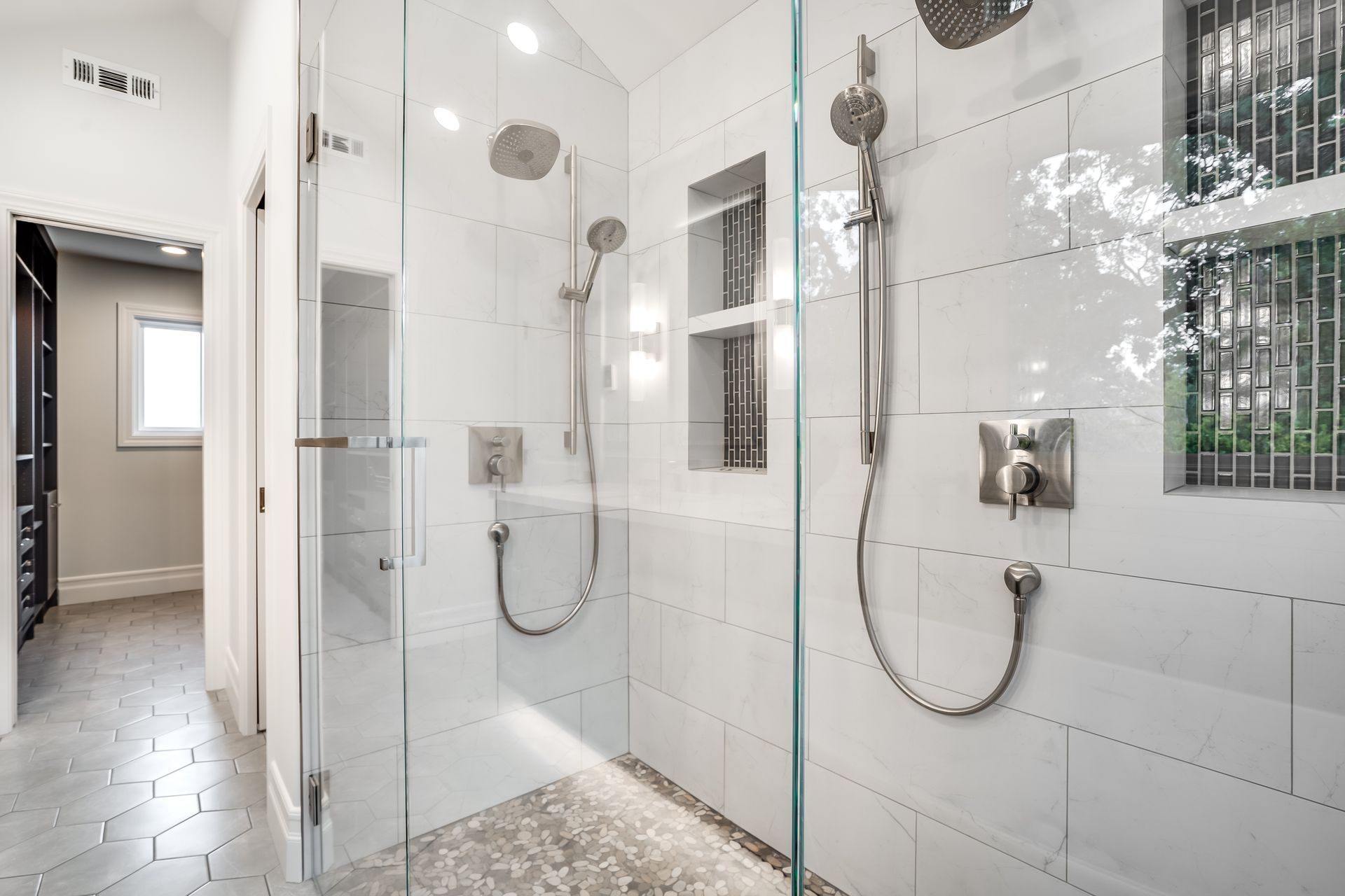 Modern white tile shower with glass doors, two shower heads, and recessed storage.