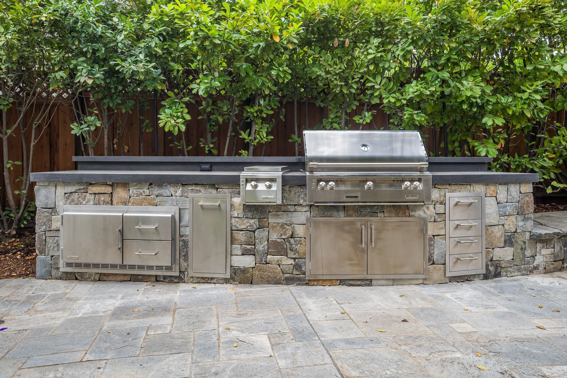 Outdoor kitchen with stainless steel grill, storage, and stone facade.