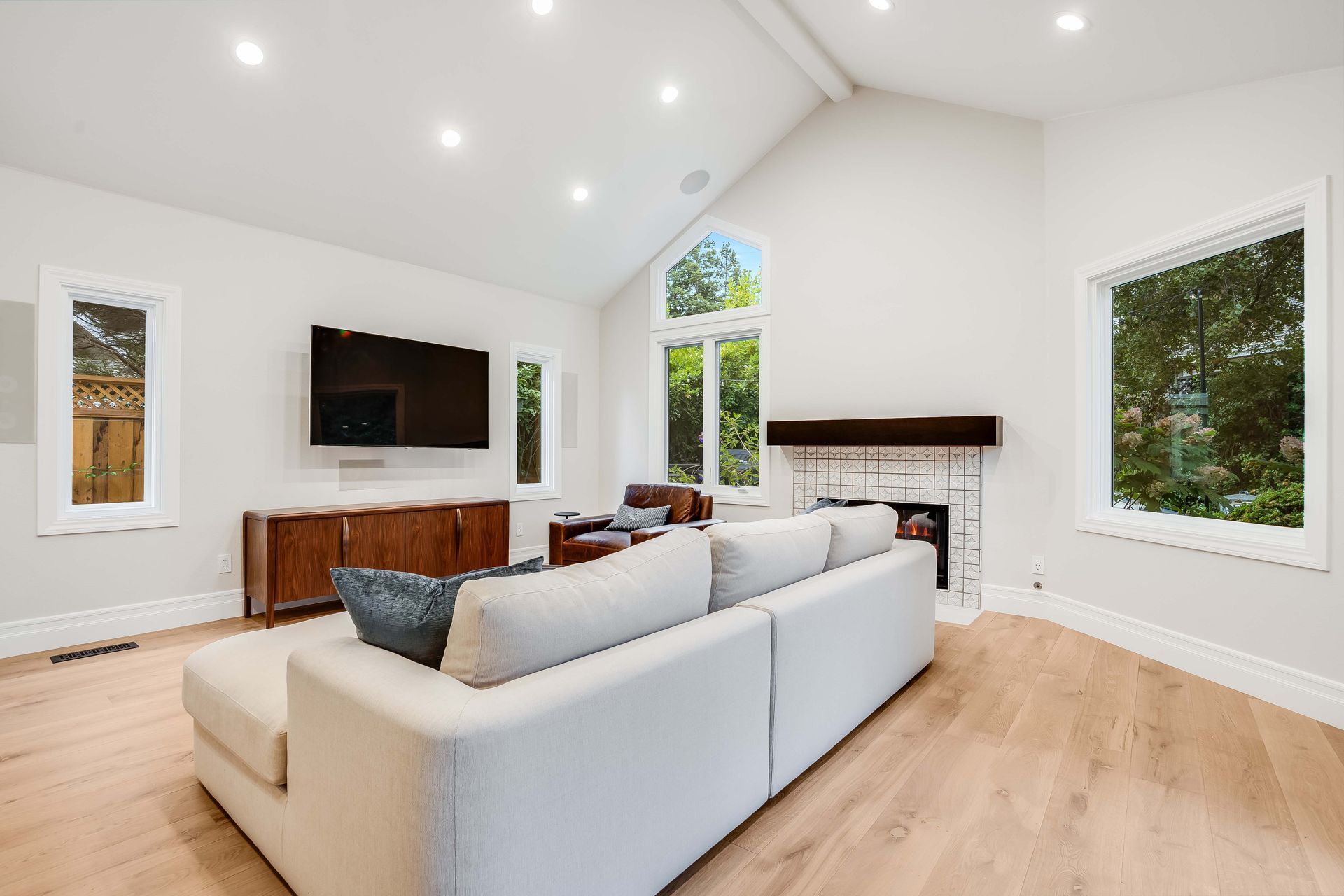 Spacious living room with vaulted ceiling, white walls, large windows, wood floors, and a modern white sofa.