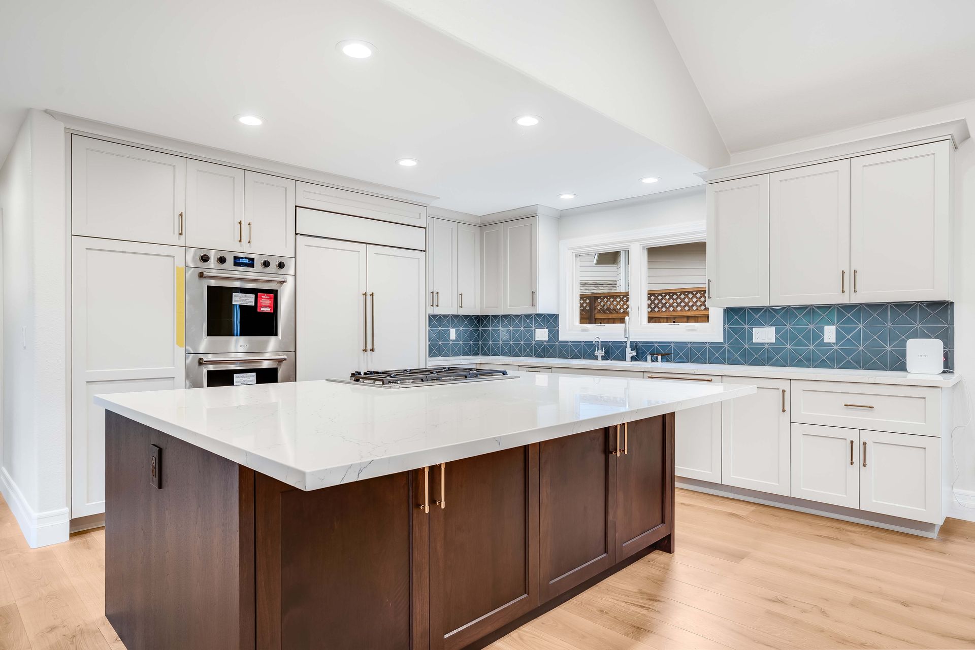 Modern kitchen with white cabinets, dark island, and blue tile backsplash.