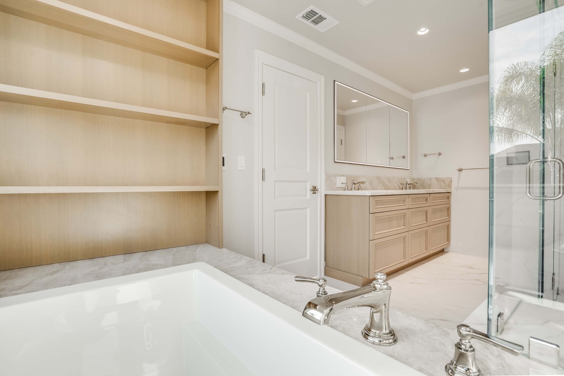 Bathroom with built-in shelves, tub, vanity, and shower. Neutral tones and marble tiles.