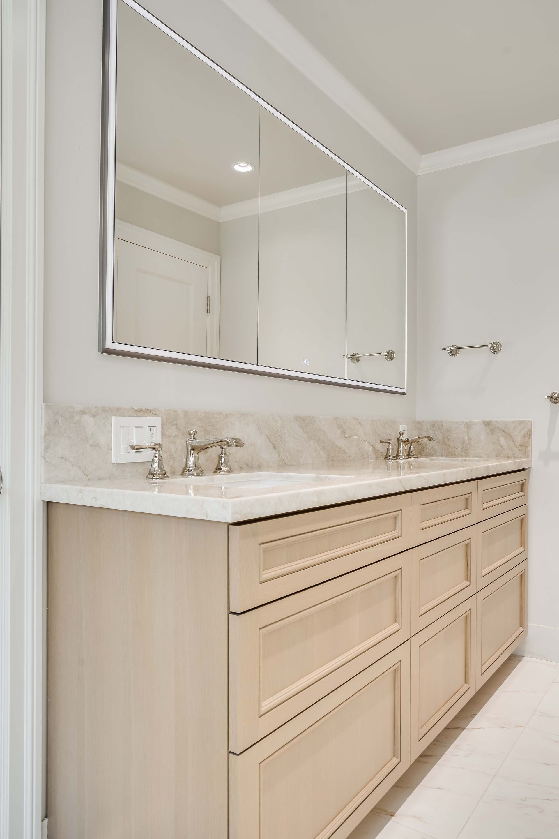 Bathroom vanity with a large mirror, light-colored cabinets, marble countertop, and chrome faucets.