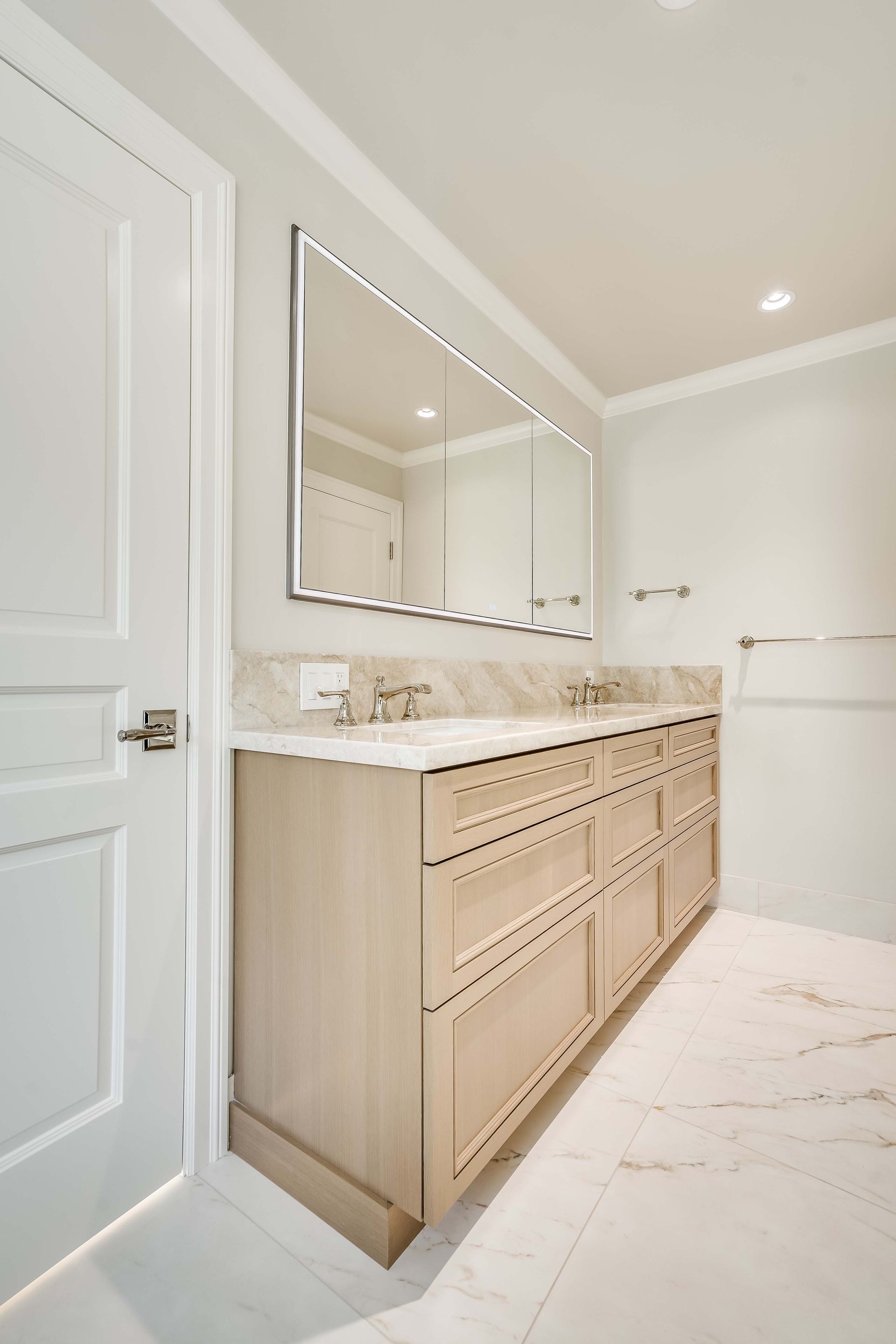 Bathroom with a light wooden vanity, marble countertop, and a large mirror.