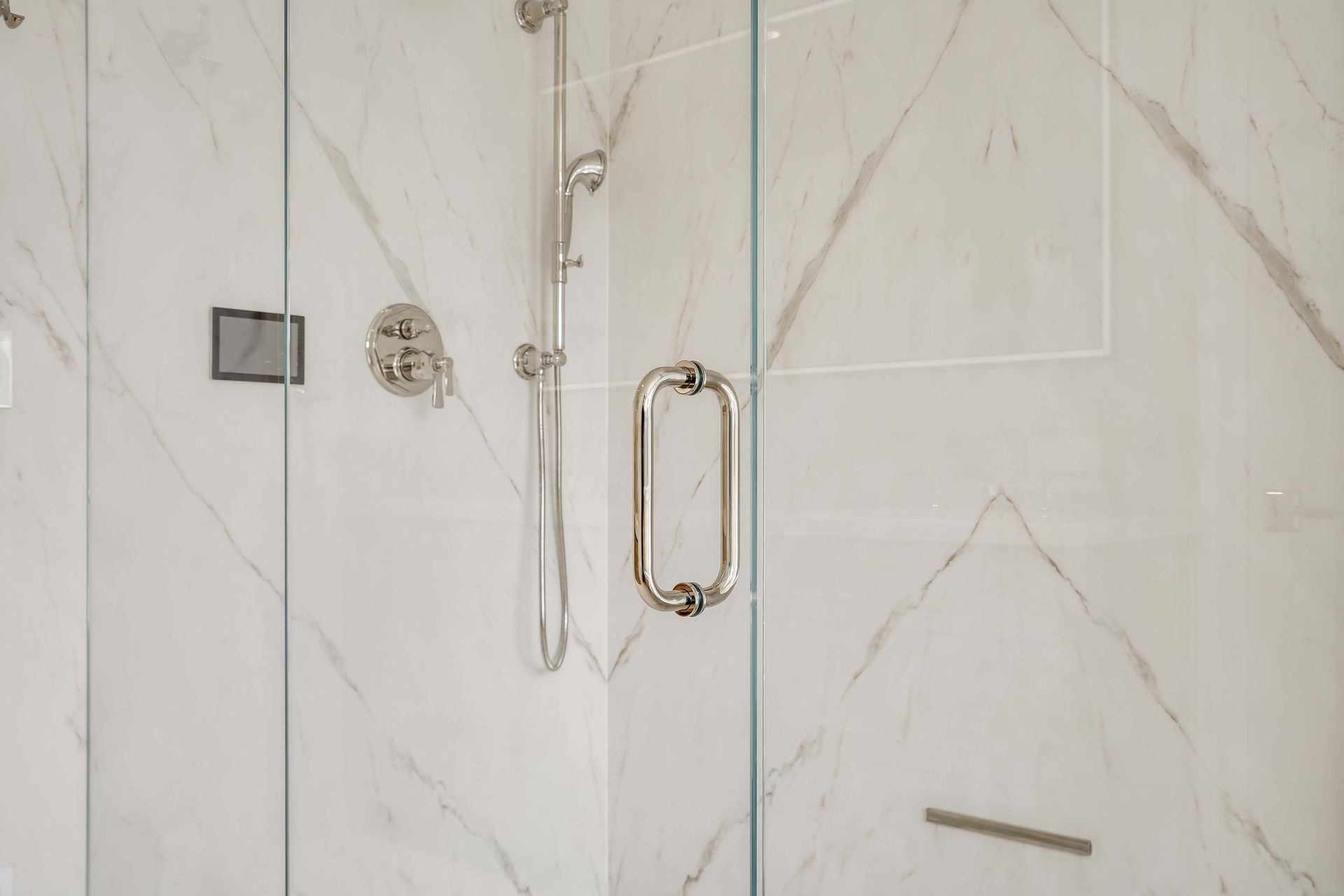 Shower stall with white marble-patterned walls and glass doors; chrome fixtures and handle.
