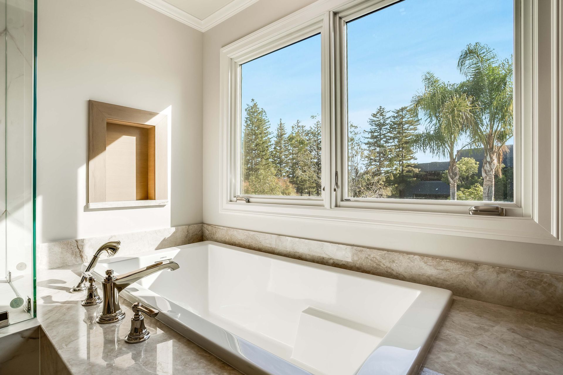 Bathroom with white tub, large window overlooking trees, and marble accents.