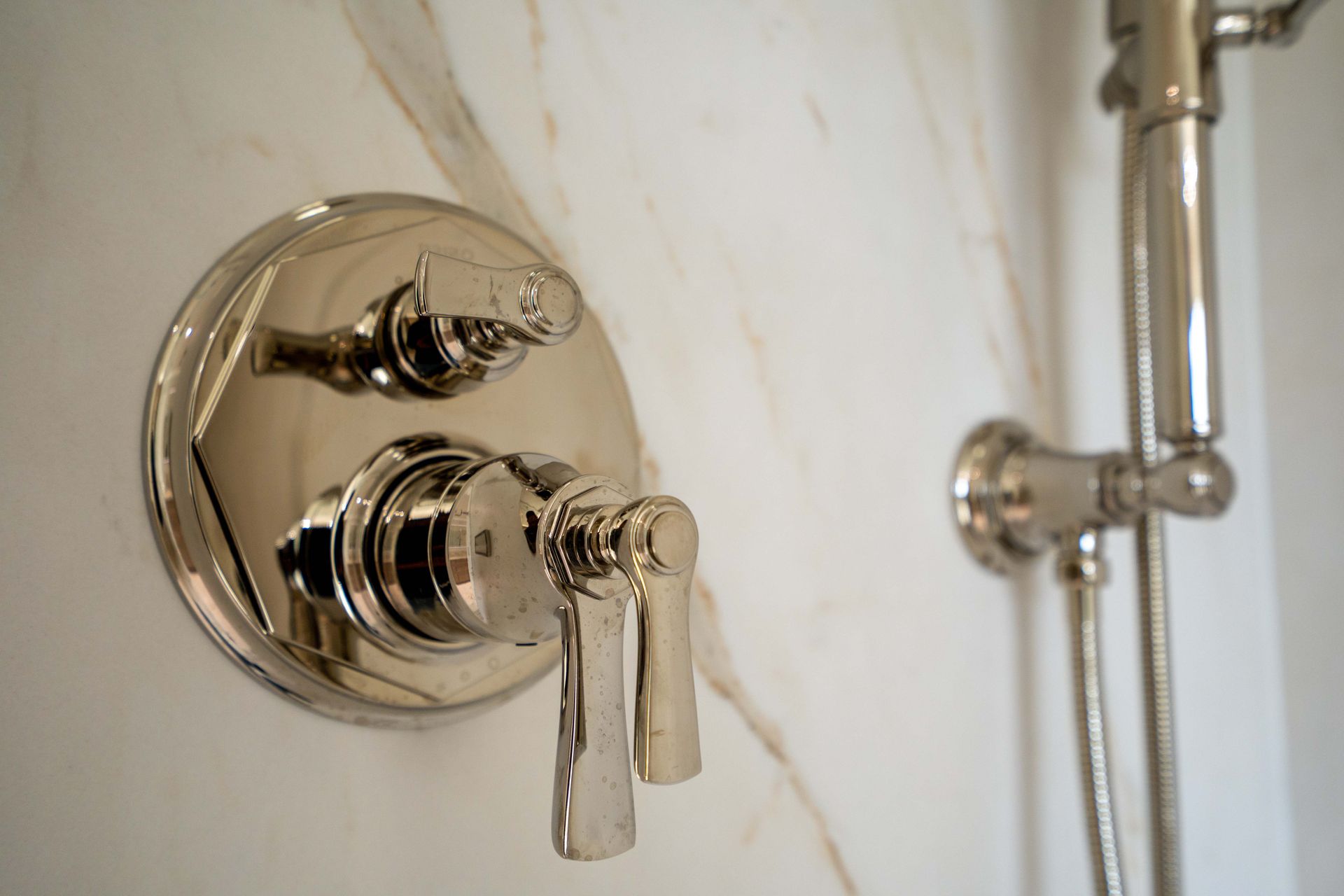Polished nickel shower fixtures on a white marble wall.