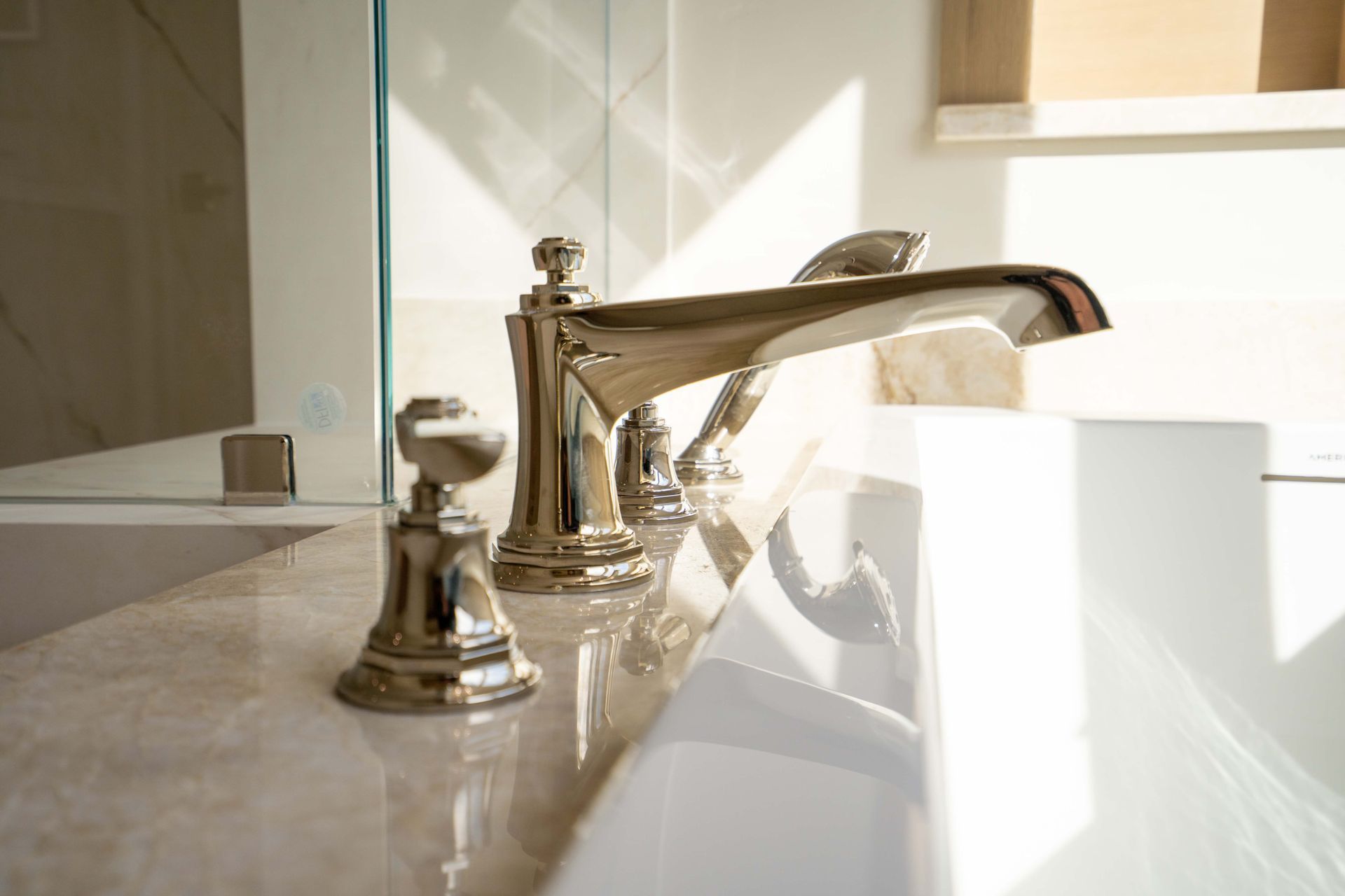 Close-up of a shiny chrome faucet on a white countertop; sunlight reflects off the fixtures.