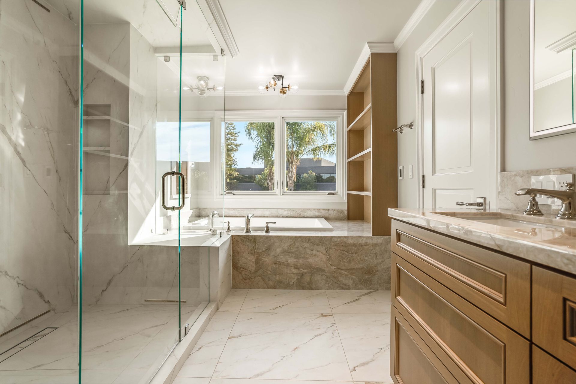Luxurious bathroom with marble tile, glass shower, and wooden vanity.