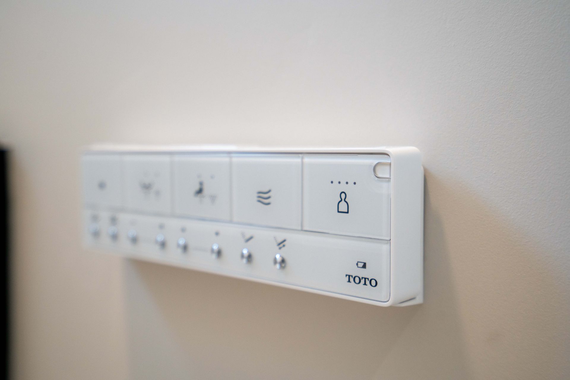 White control panel mounted on a beige wall, with multiple buttons and a