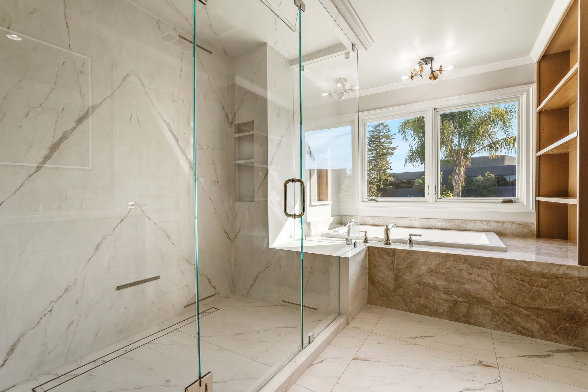 Luxurious bathroom with marble walls, glass shower, and large window.