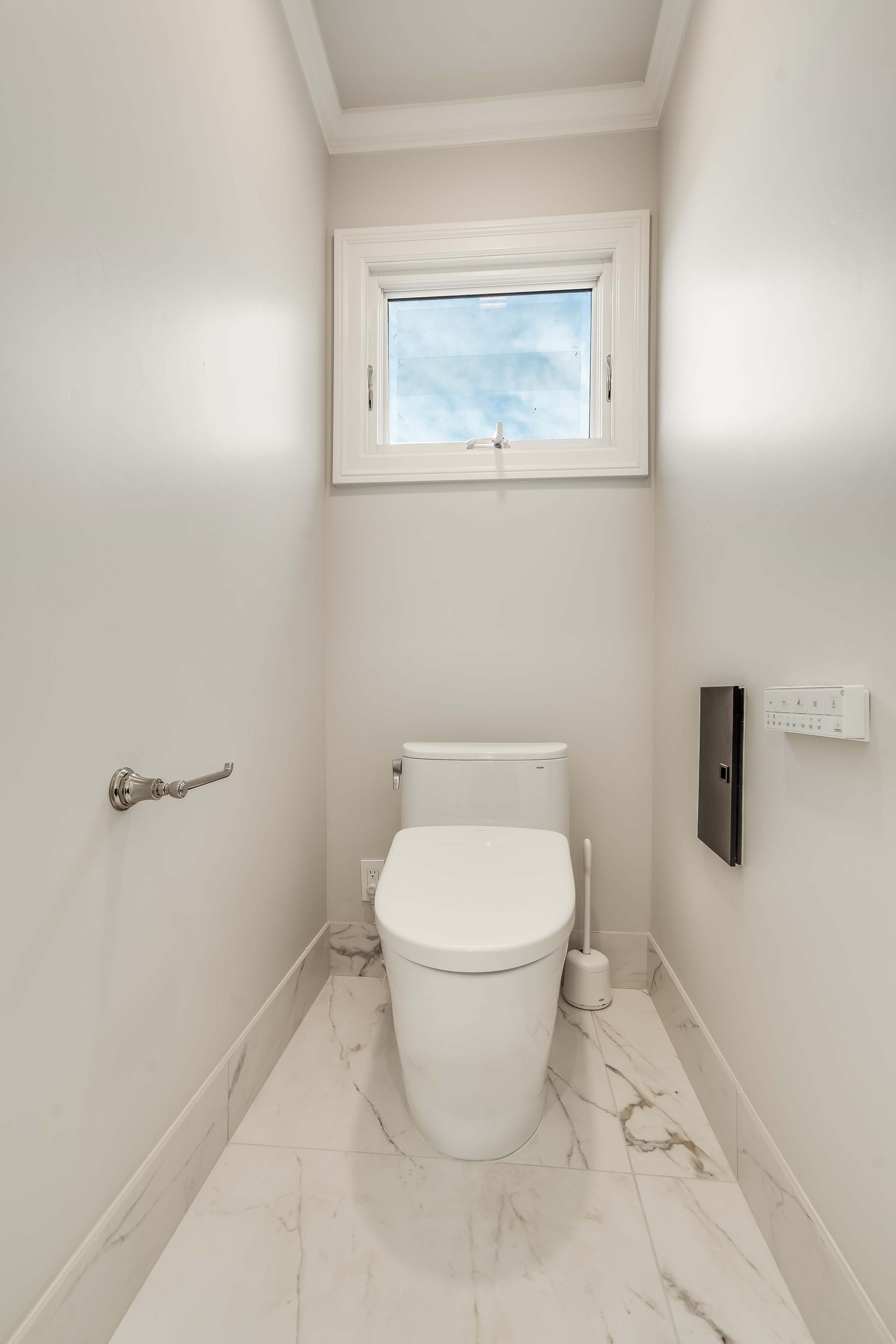 Small, white bathroom with a toilet, window, and marble flooring.