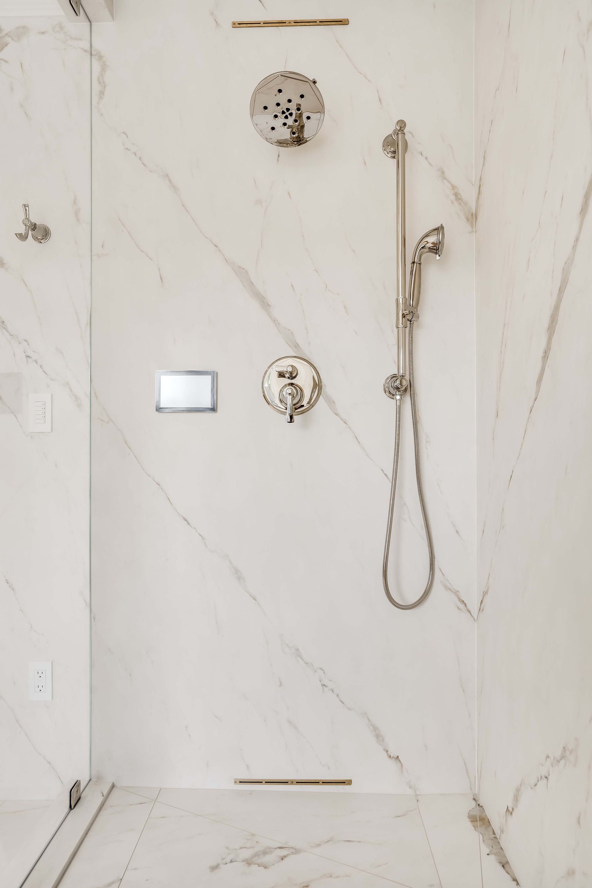 White tiled shower with silver fixtures, including showerhead, hand-held sprayer, and faucet controls.