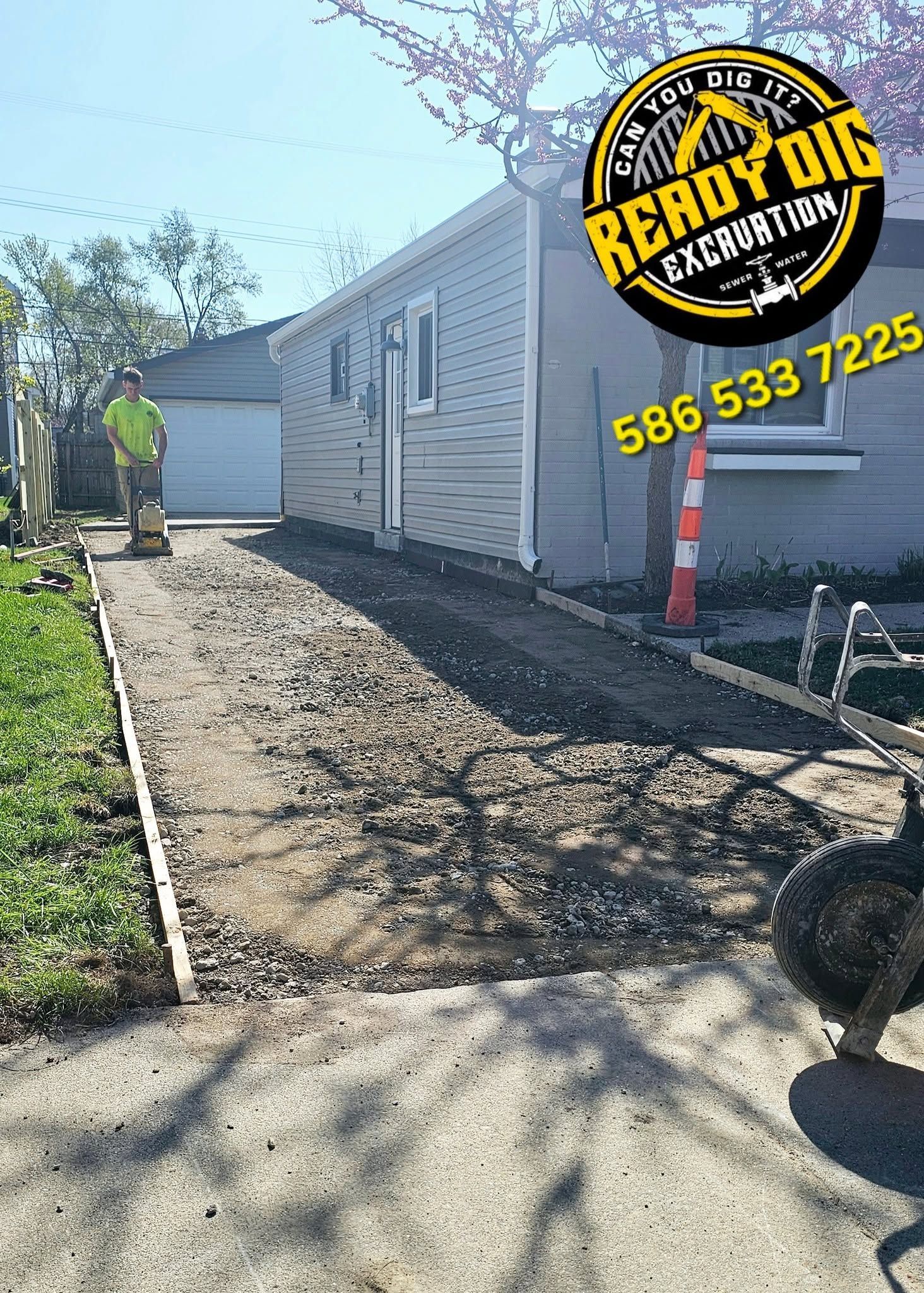 Gravel walkway beside a white house under construction, with a worker in the distance and a Ready Mix sign.