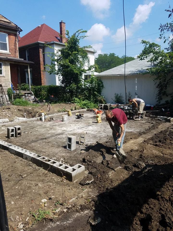 Workers leveling a backyard construction site beside a brick house under a bright blue sky