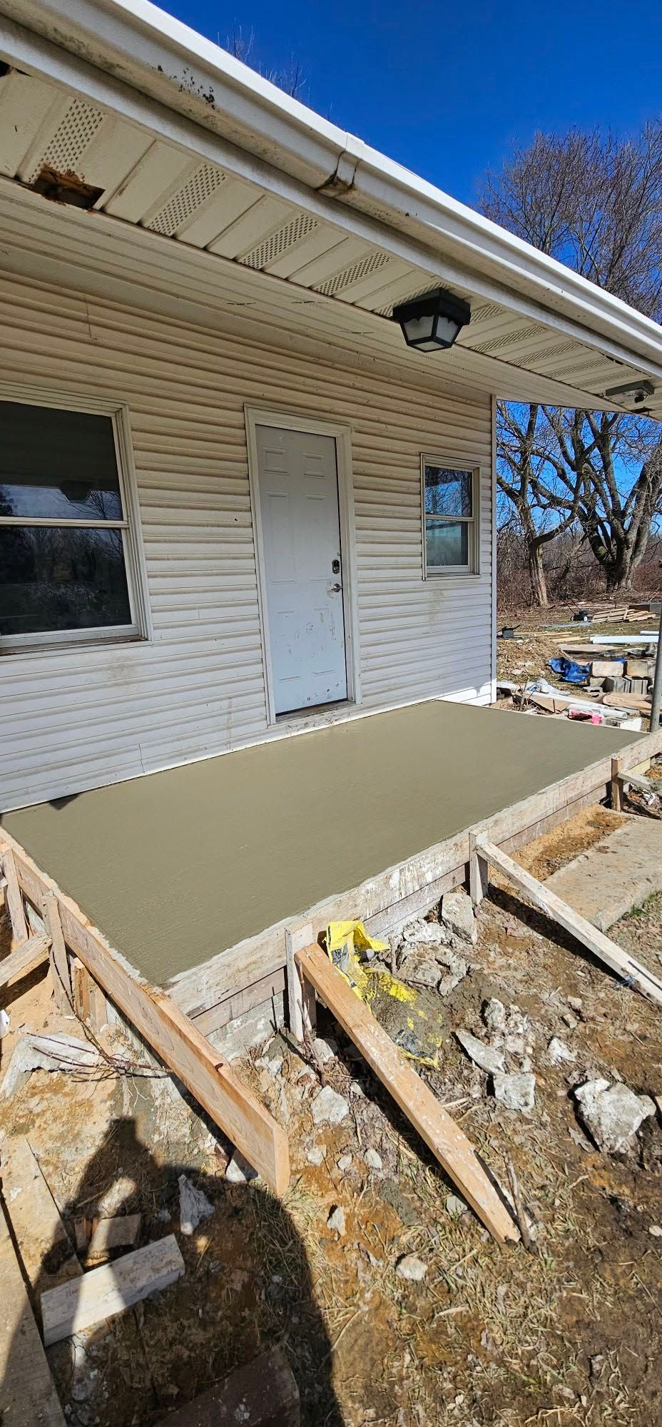 House exterior with a small gray concrete porch under construction and wooden formwork in front.