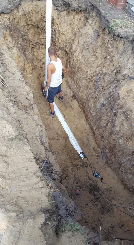 Worker standing in a deep trench beside a white pipe