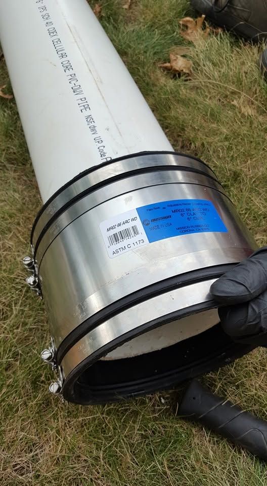Metal duct pipe with blue label and black connector rings on grass, held by a gloved hand.