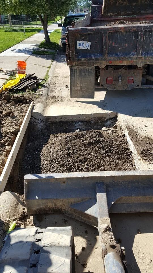 Construction truck dumping asphalt into a road trench beside orange cones and tools