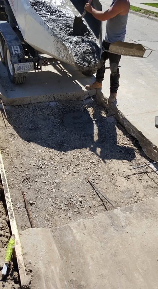 Worker pouring wet concrete onto a sidewalk repair area beside a curb.