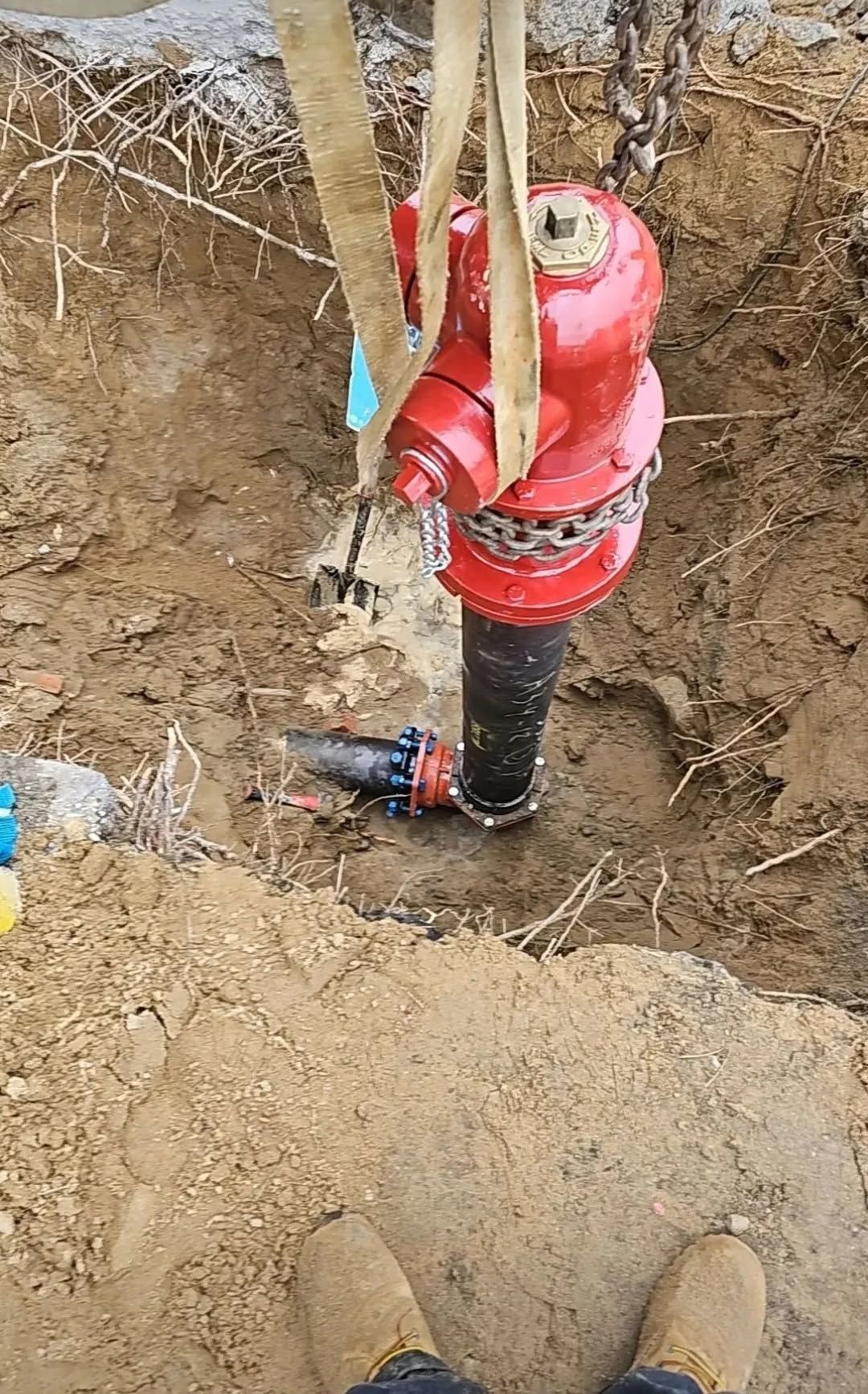 Utility pipe with red valve cap in a dirt excavation, viewed from above.