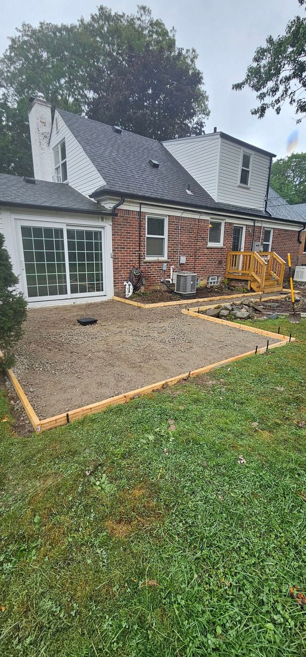 Small brick house with a gravel patio, patio furniture, and a yellow excavator in the yard.