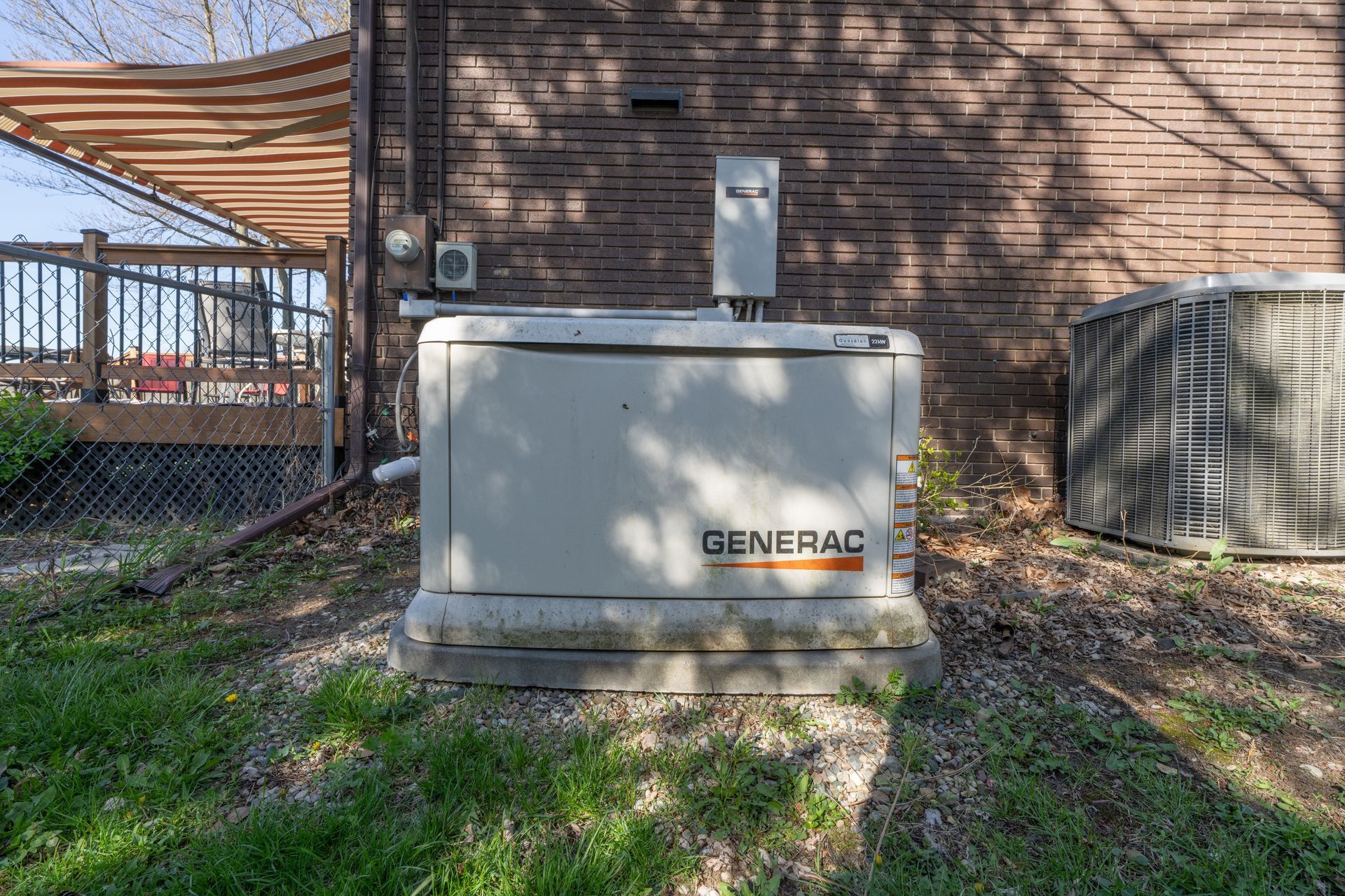 Outdoor Generac generator beside a brick house, with grass and an HVAC unit nearby