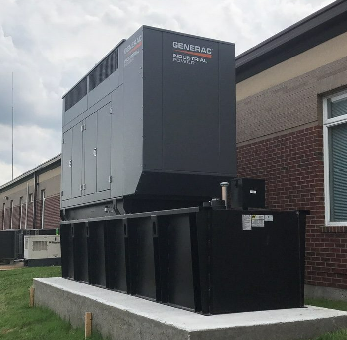 Large gray industrial HVAC unit on black platform beside a brick building outdoors