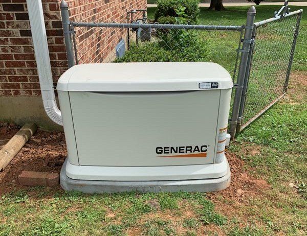 Generac outdoor standby generator beside a brick house and chain-link fence
