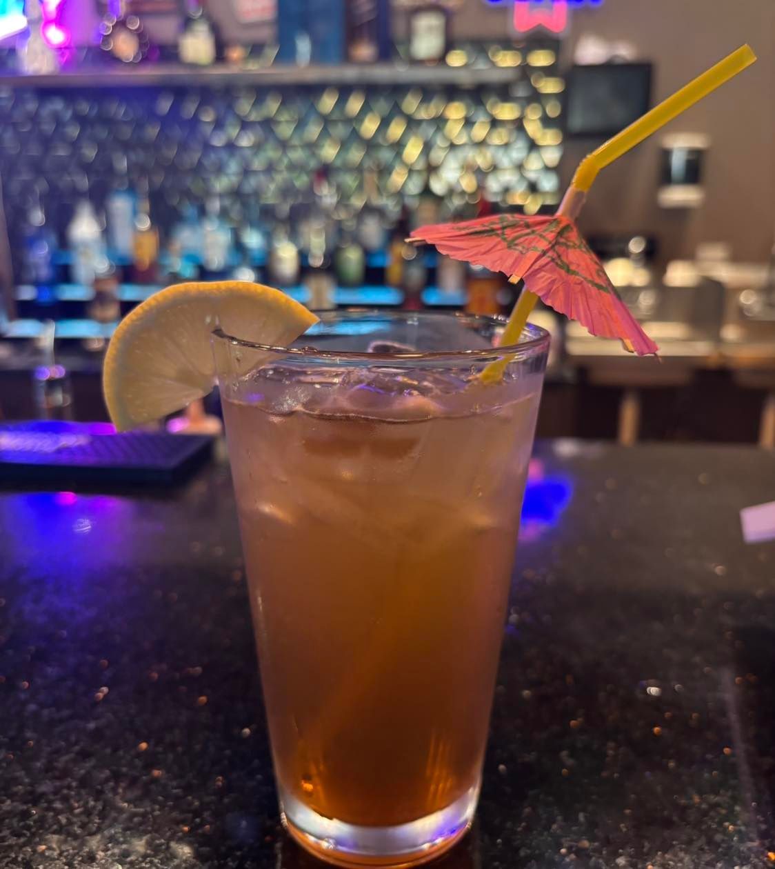 Tropical cocktail with a lime wedge and paper umbrella on a bar counter, blurred bar lights behind