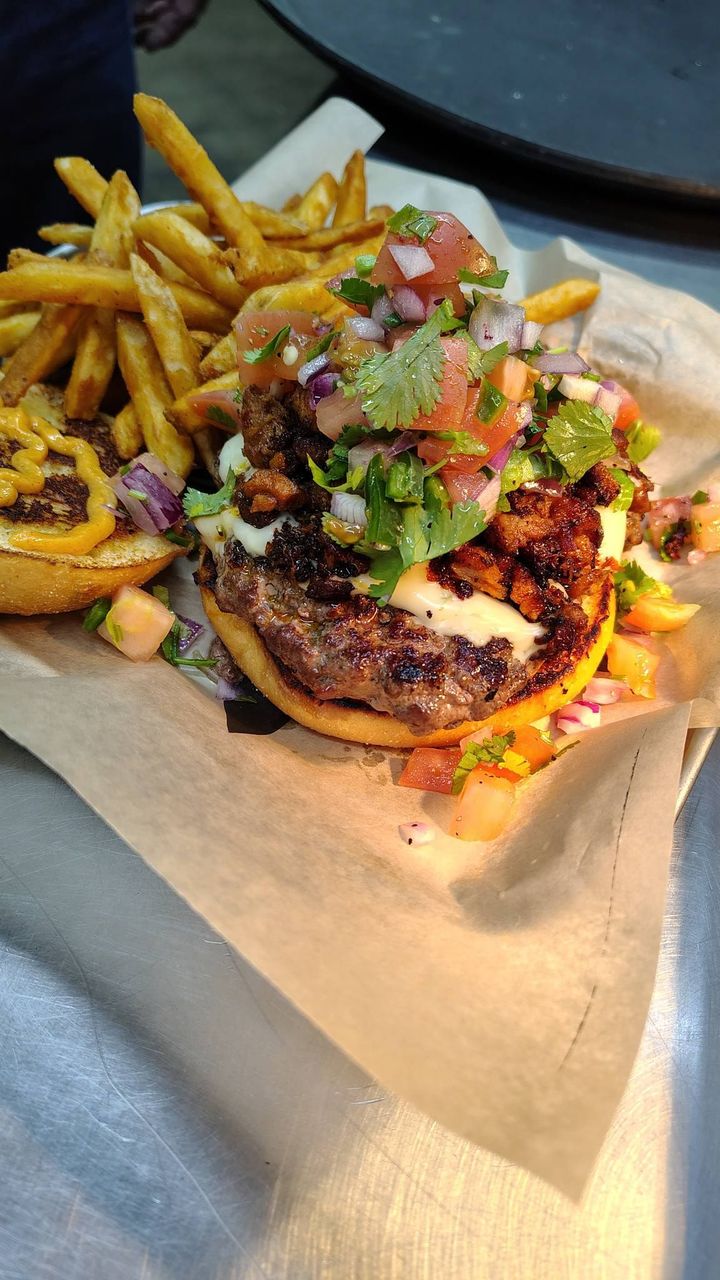 Burger topped with salsa and greens beside French fries on a paper-lined tray