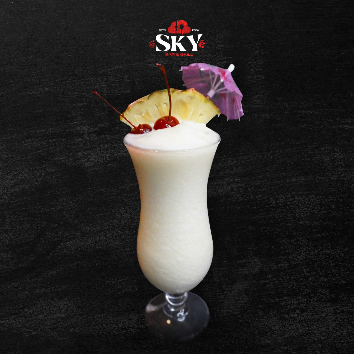 Tall creamy tropical cocktail with pineapple slice, cherry, and purple umbrella on a dark background
