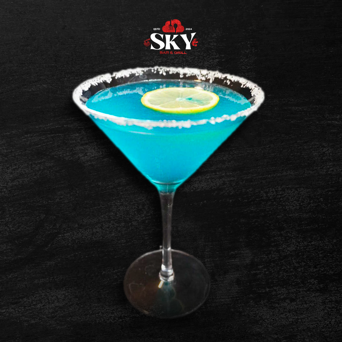 Blue cocktail in a martini glass with a lemon slice and salted rim on a dark background.