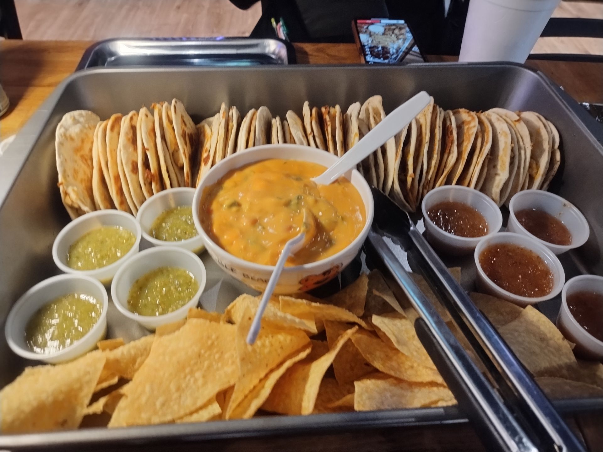 Tray of tacos, tortilla chips, and salsa cups with a central bowl of queso dip.