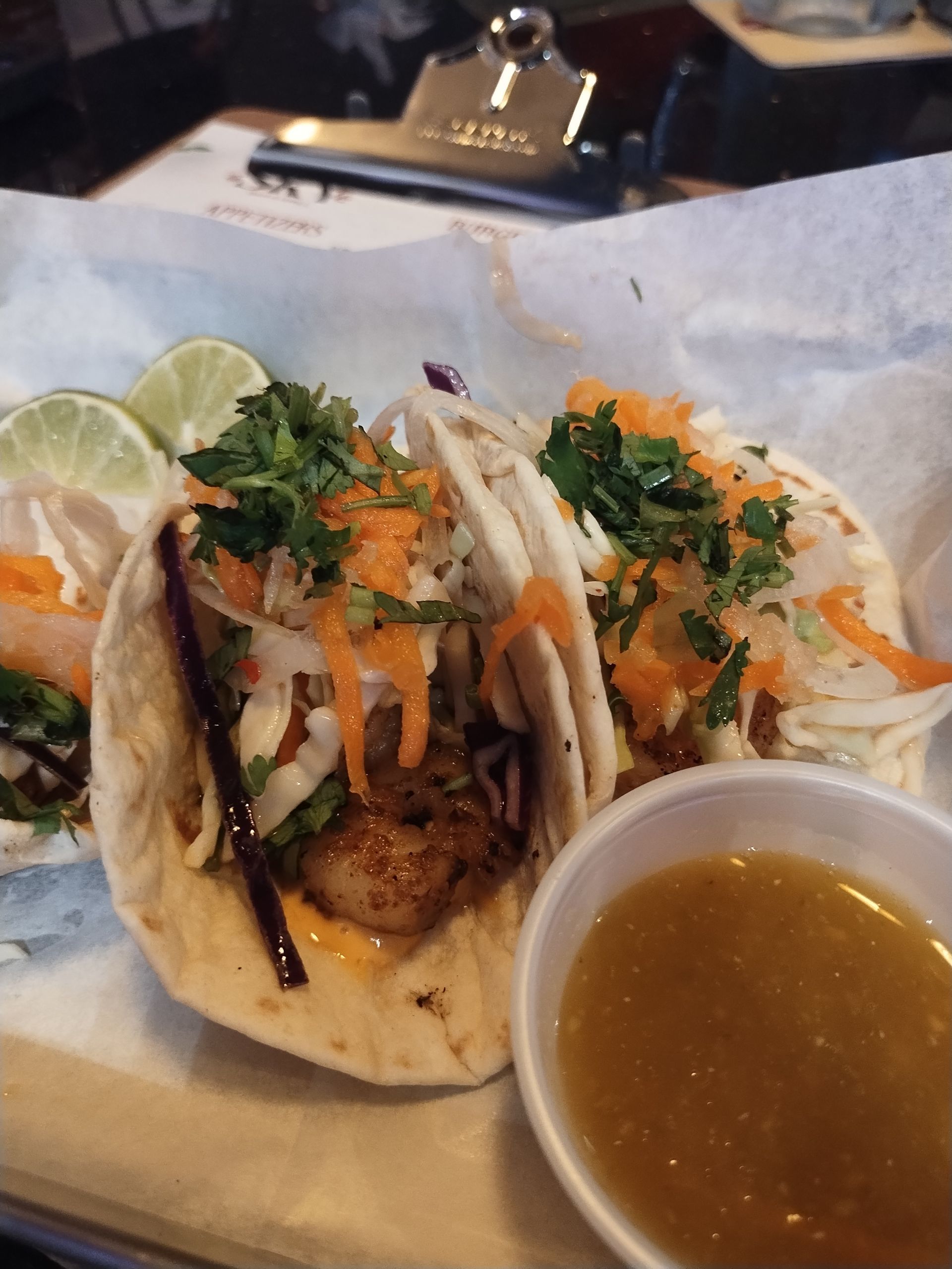 Tacos with lime wedges and salsa on a plate, topped with onions and cilantro.