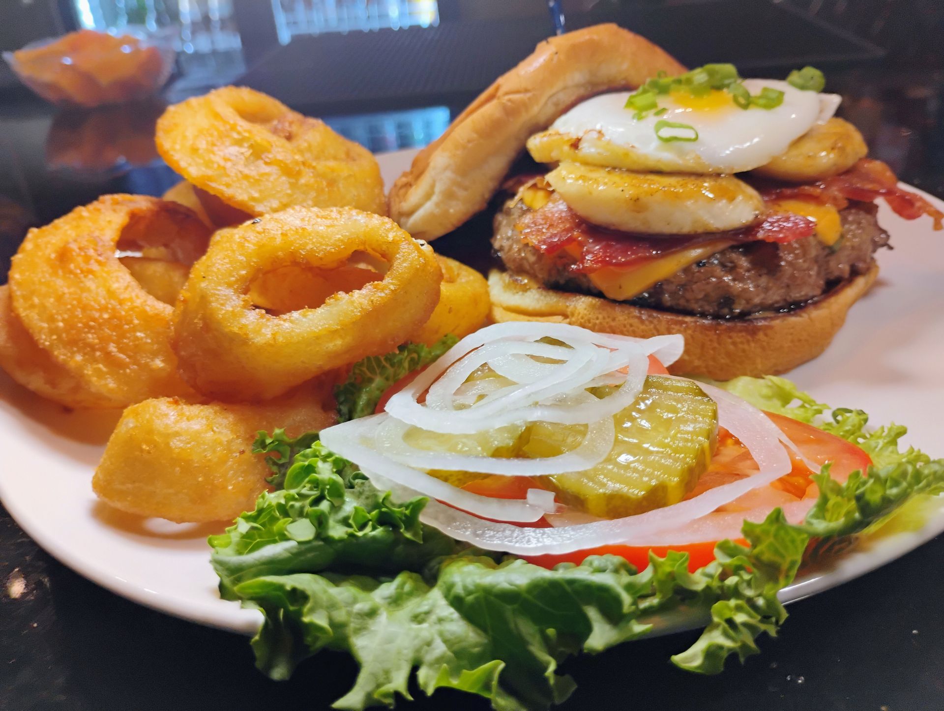 Burger with onion rings, fries, and a side salad on a white plate
