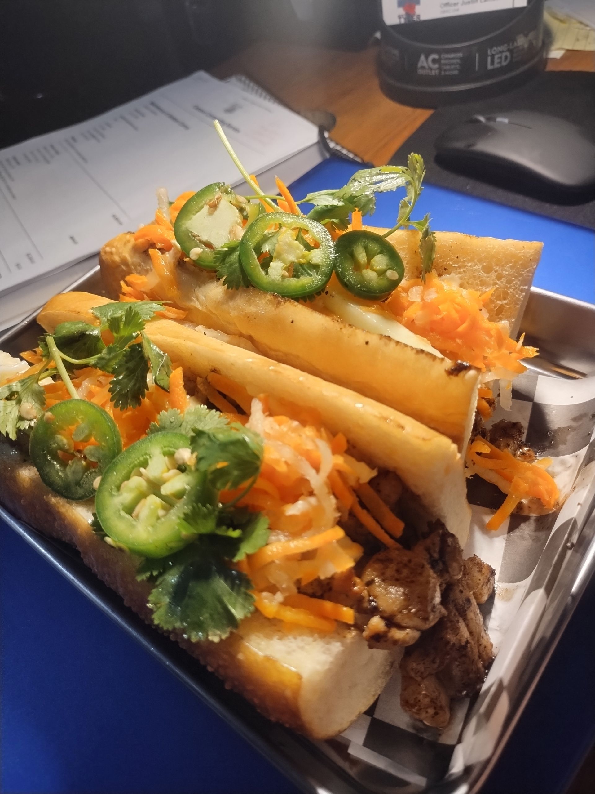 Loaded sandwich with fries, shredded carrots, cilantro, and sliced jalapeños in a takeout box