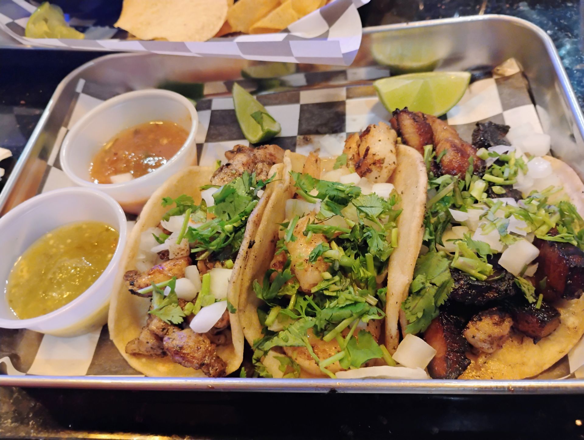 Tray of tacos with lime wedges and two dipping sauces on a checkered tablecloth