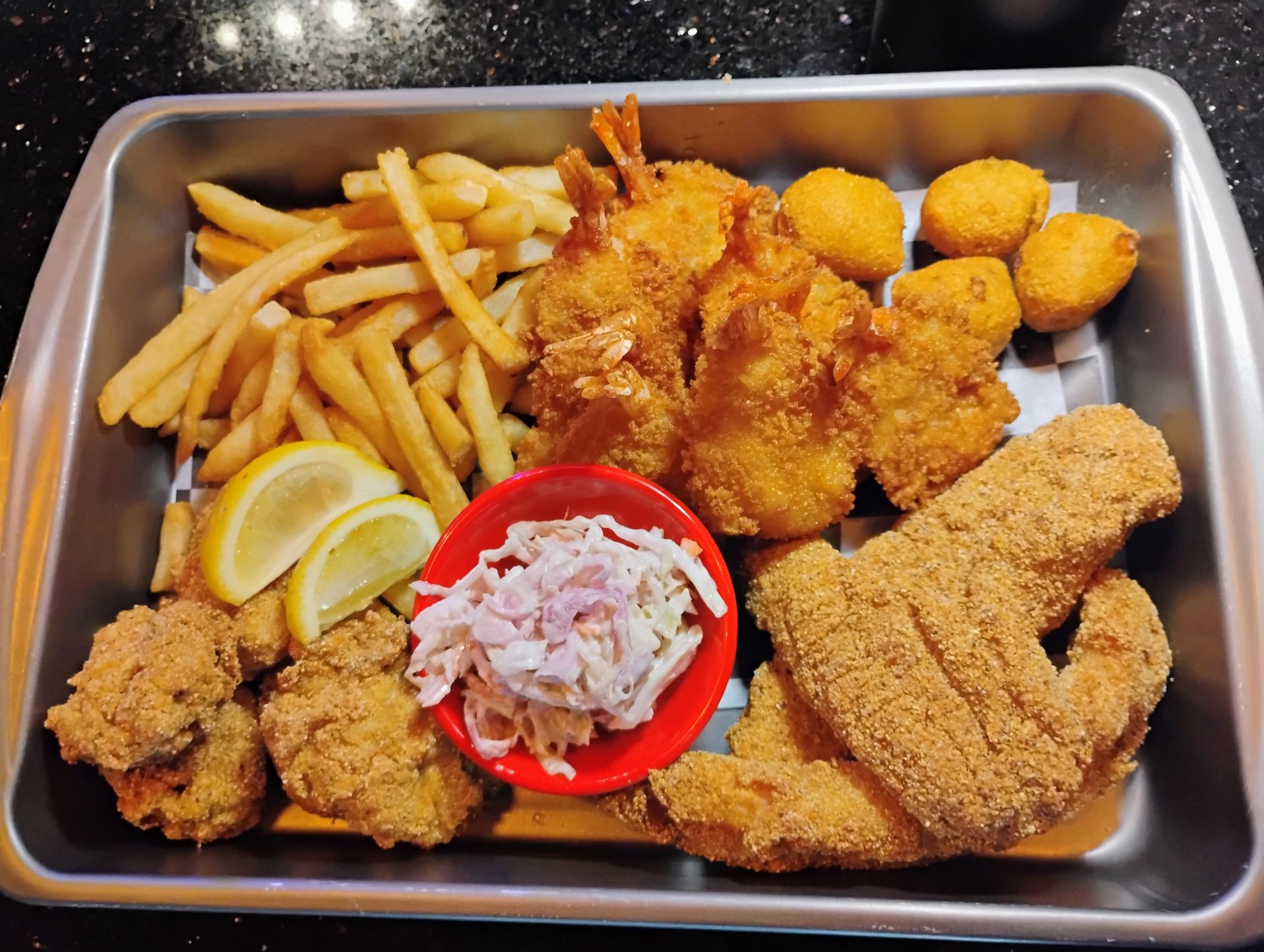 Tray of fried chicken, French fries, lemon wedges, and coleslaw in a takeout container