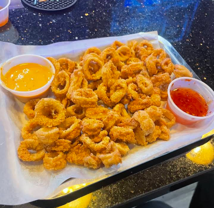 Tray of golden fried calamari rings with marinara and cheese dipping sauces on a table.