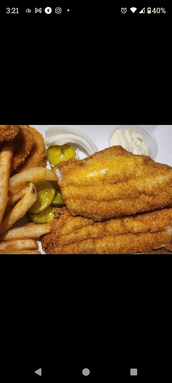 Golden fried fish fillets with potato wedges and pickles on a plate, with dipping sauce.