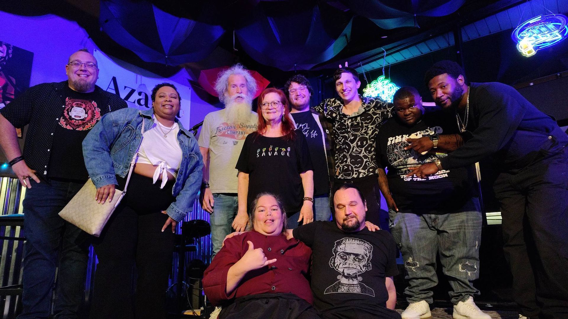 Group of smiling people posing on a stage with blue lighting and draped backdrop
