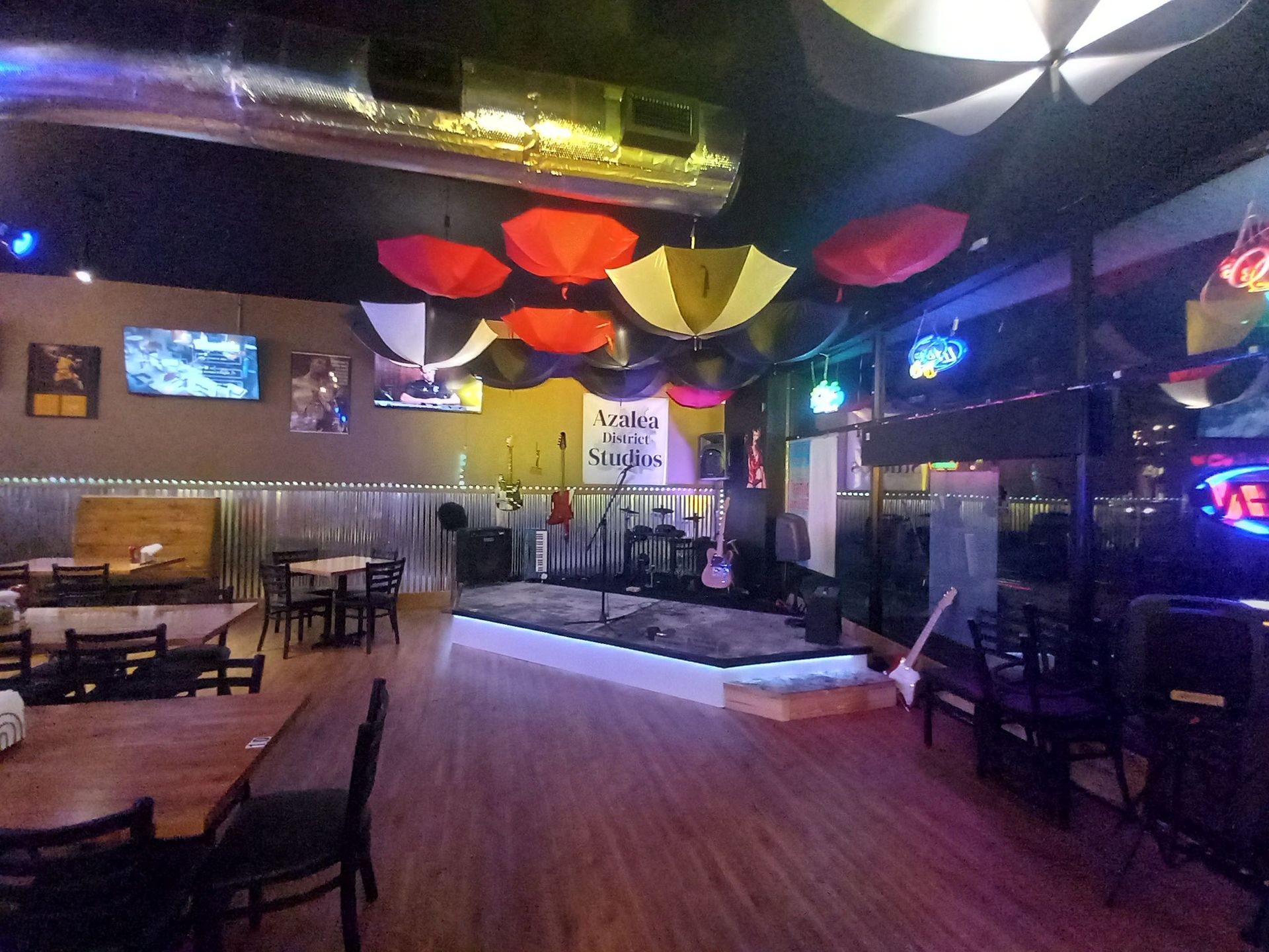 Colorful lounge interior with tables, chairs, stage, hanging umbrellas, and neon lights