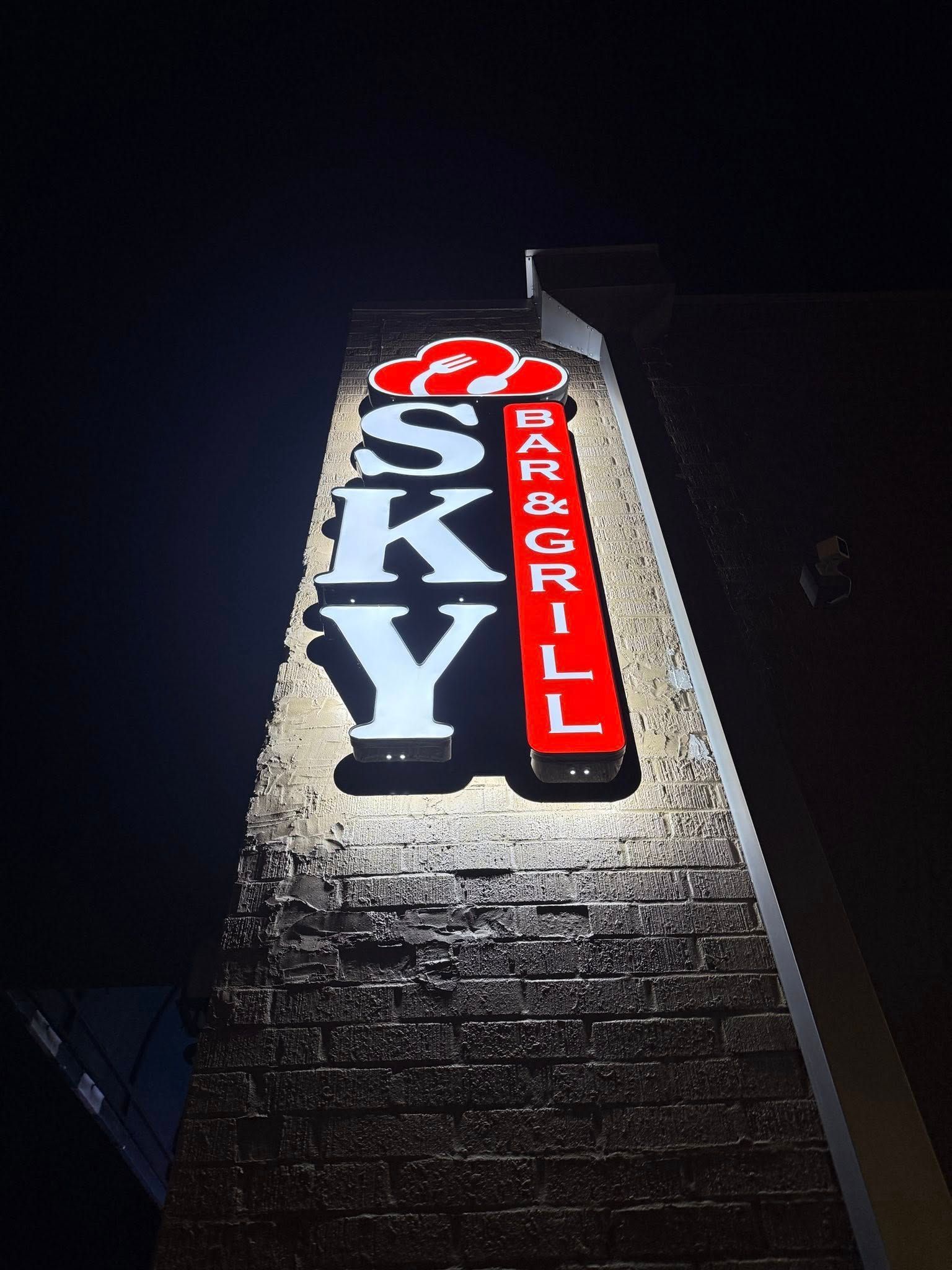 Illuminated SKY Bar Grill sign on a brick building at night