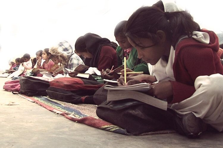 A group of children are sitting on the ground writing in notebooks